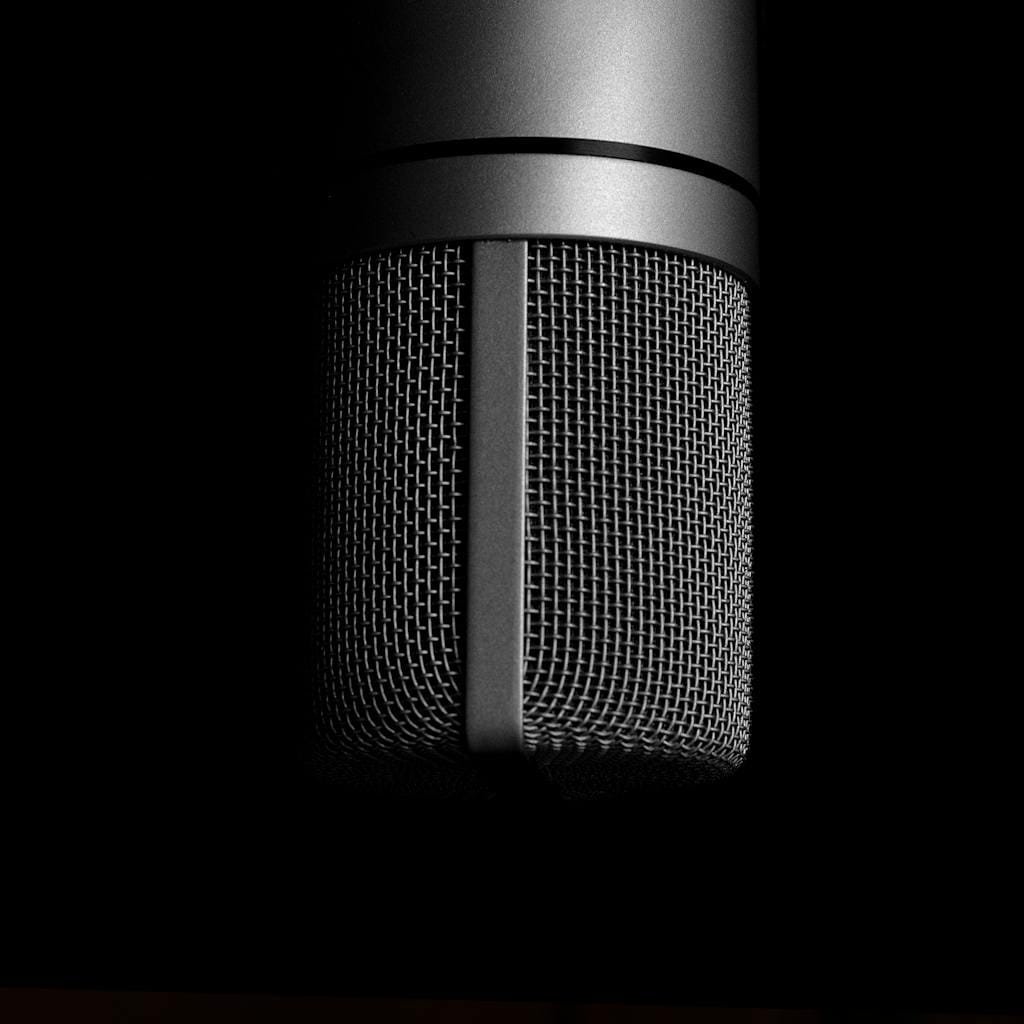 Detailed close-up shot of a metallic studio microphone on a black background, emphasizing sound recording equipment.